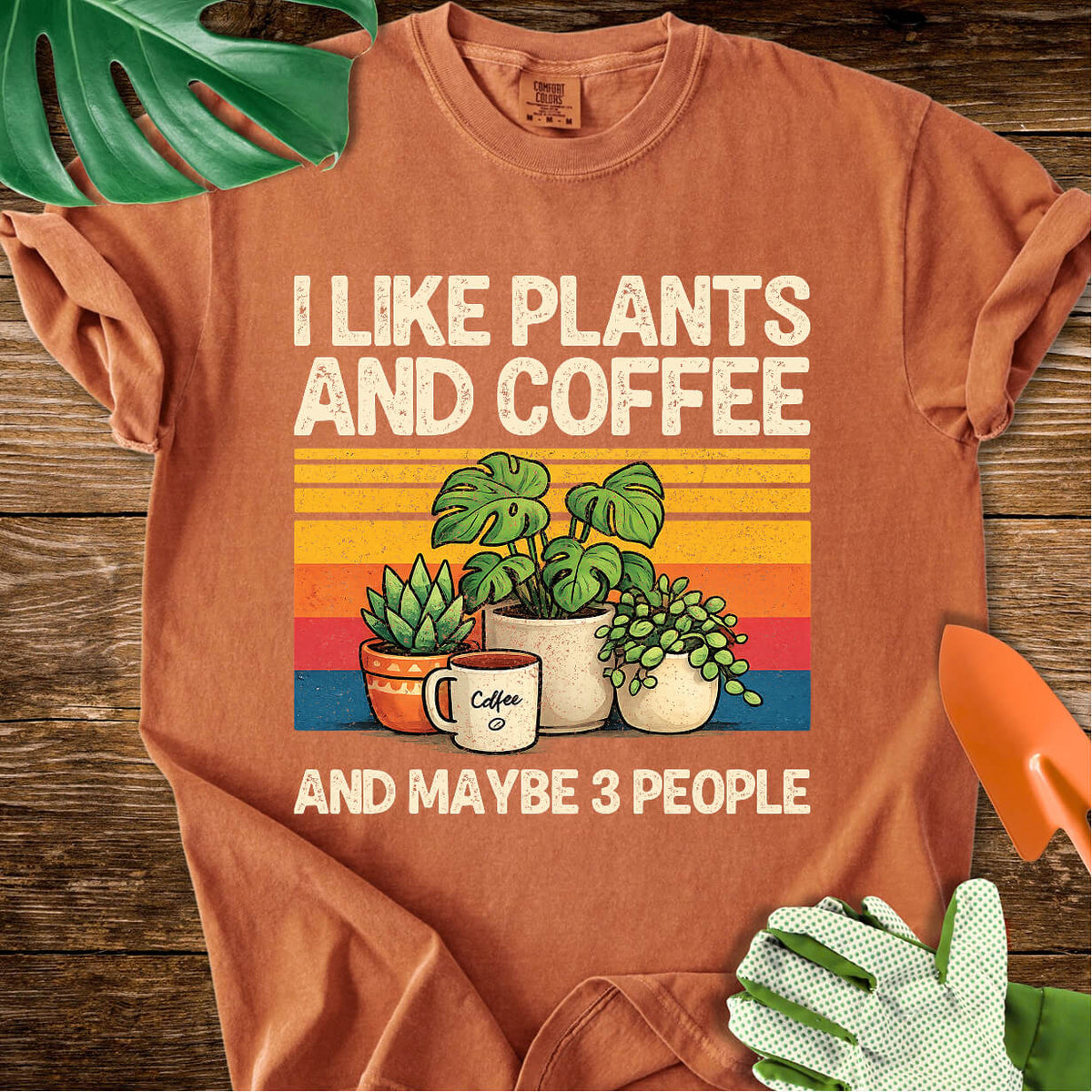 Burnt orange Comfort Colors T-shirt with plants, coffee, and retro stripes with "I Like Plants and Coffee and Maybe 3 People".