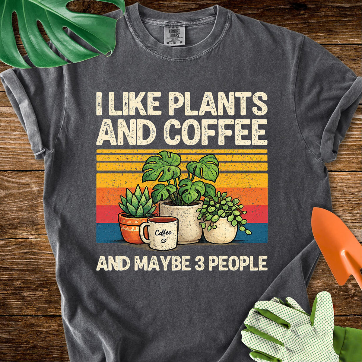 Pepper charcoal gray Comfort Colors T-shirt with plants, coffee, and retro stripes with "I Like Plants and Coffee and Maybe 3 People".